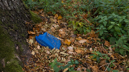 Obraz premium Environmental pollution. An old blue plastic canister from gasoline lies in the forest by a tree among the leaves. Toxicity. Soil contamination with hydrocarbons. Ecology.