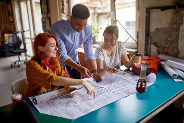 A group of young creative colleagues in the office is enjoying working together on a new guitar design