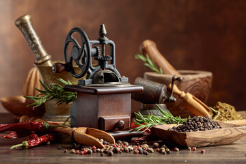 Vintage pepper mill with kitchen utensils, spices and rosemary on a old wooden table.