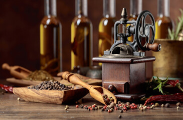 Old pepper mill with cooking utensils, bottles of olive oil, spices and rosemary on a wooden table.