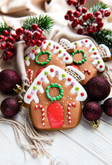 Homemade gingerbread houses  fir-tree branches and berries on white wooden table.