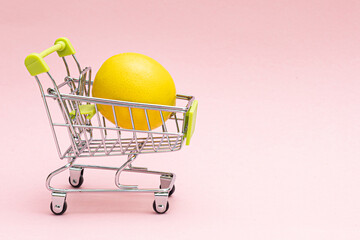 Shopping cart with lemon on a pink background. Grocery and grocery store concept.