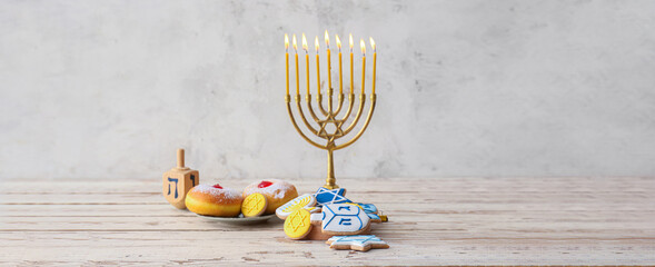 Tasty cookies and donuts for Hanukkah celebration with menorah on light background with space for...