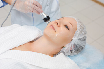 Close up portrait of a beautiful smiling woman relaxing during the RF lifting procedure in a modern beauty salon