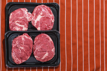 Rib eye steaks on a black plastic tray on red and white apron. Premium beef product. Fresh meat. Butcher craft. Food supply industry.