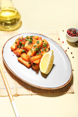 Plate with honey chilli potato and chopsticks on light background