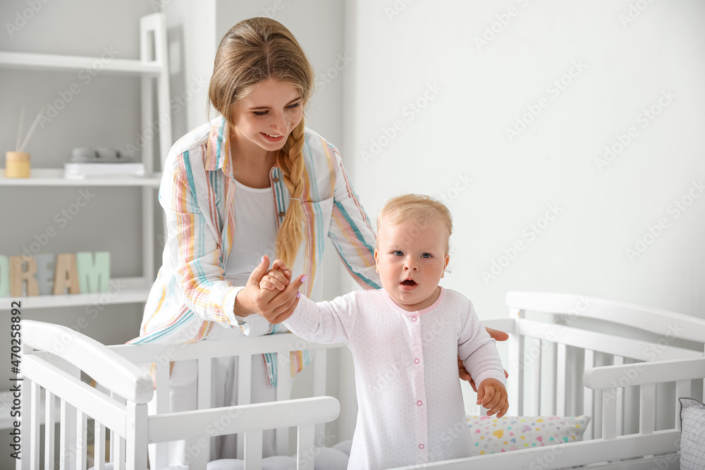 Wall mural Young mother and her cute little baby in crib