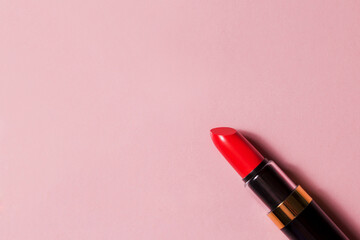 Fototapeta premium Red lipstick in a black package on a pink background with space for text. Cosmetics top view