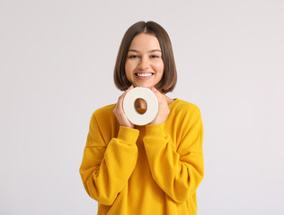 Young woman with toilet paper on light background