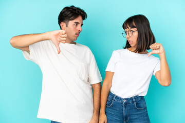 Young mixed race couple isolated on blue background showing thumb down sign with negative expression
