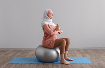 Pregnant Muslim woman with fitball meditating in gym