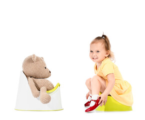 Cute baby girl and toy bear sitting on potties against white background