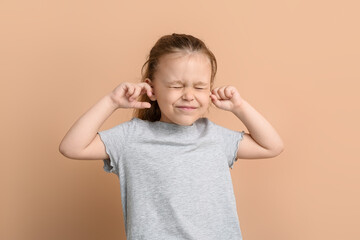 Portrait of pretty little girl plugging ears on color background