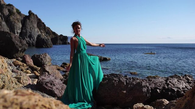 Side view a Young beautiful sensual woman with black hair in a long mint dress posing on a beach with calm sea bokeh lights on sunny day. Girl on the nature on blue sky background. Fashion photo