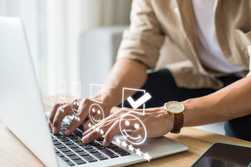 Businessman using laptop and pressing face emoticon on the keyboard and selecting smiley face icon and a 5 star rating. Demonstrates that customer satisfaction is essential to a successful business.