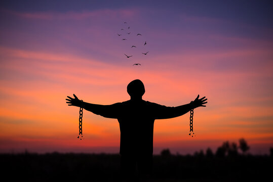 Silhouette of young man standing alone  with beautiful sky at sunset open both arms with chains on his arms. He felt free from the shackles tied to his arms.