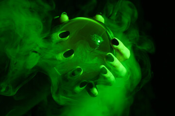Witch holding crystal ball in green smoke on dark background