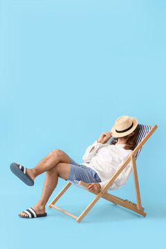 Handsome young man sitting on deck chair against color background