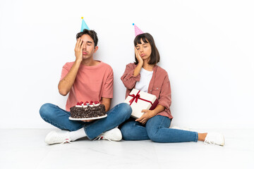 Young mixed race couple celebrating a birthday sitting on the floor isolated on white background with surprise and shocked facial expression