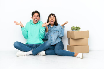 Young couple making a move while picking up a box full of things sitting on the floor isolated on white background with surprise and shocked facial expression