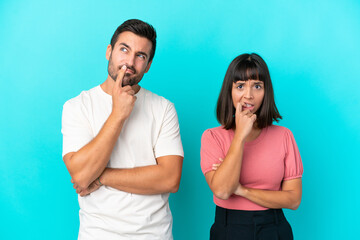 Young couple isolated on blue background having doubts while looking up