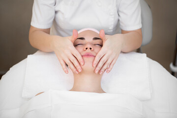 Obraz na płótnie Canvas Beautician makes a professional massage of the face of the neck and shoulders for a young girl in the Spa salon. The view from the top. Facial beauty treatment