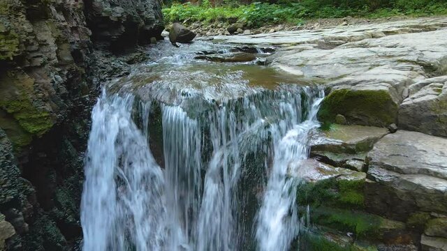 Waterfall on mountain river with white foamy water falling down from rocky formation in summer forest