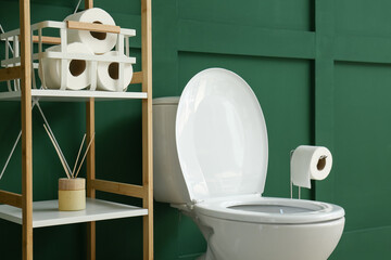 Toilet bowl and shelving unit near green wall