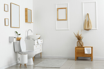 Interior of light restroom with toilet bowl and chest of drawers