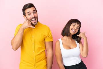 Young couple isolated on pink background making phone gesture. Call me back sign