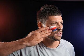 Handsome man with flag of Russia painted on his face against dark background