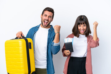 Young traveler couple holding a suitcase and passport isolated on white background celebrating a...