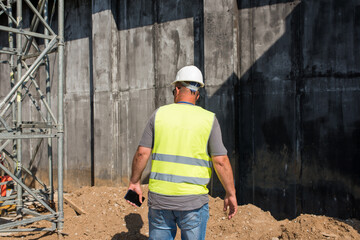 Foreman in a safety helmet and a vest with a telephone at a construction site