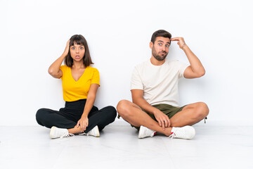 Young couple sitting on the floor isolated on white background with an expression of frustration and not understanding