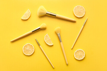 Stylish makeup brushes and lemon on yellow background