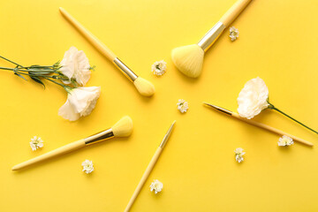 Makeup brushes and flowers on yellow background