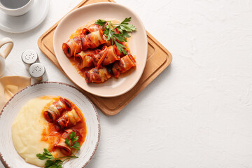 Plates with mashed potatoes, prunes baked in crispy bacon, gravy sauce and parsley on white table