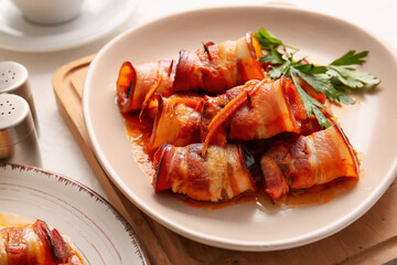 Plate with delicious prunes baked in crispy bacon and gravy on wooden board, closeup