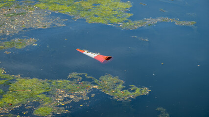 An orange traffic cone floating in a eutrophic river water after being thrown in