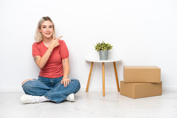 Young woman moving in new home among boxes isolated on white background pointing finger to the side