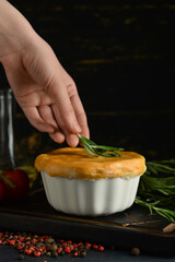 Woman decorating tasty vegetable pot pie with rosemary on black background
