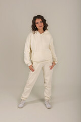 Fototapeta premium a young beautiful brown-haired girl in a warm milk-colored tracksuit white background