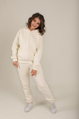 a young beautiful brown-haired girl in a warm milk-colored tracksuit white background