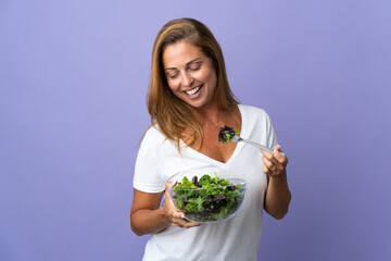 Middle age brazilian woman isolated on purple background holding a bowl of salad and looking at it with happy expression