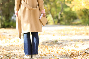 Young woman holding book in autumn park on sunny day