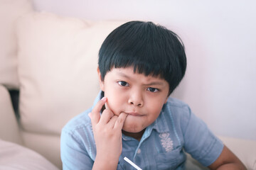 An Asian young boy nervously biting his nails.