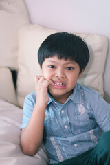 An Asian young boy nervously biting his nails.
