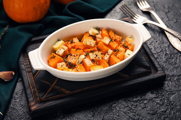 Baking dish with tasty roasted pumpkin on black background
