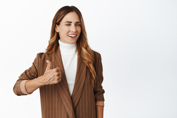 Successful businesswoman, saleswoman winking and smiling, showing thumbs up in approval, praise...