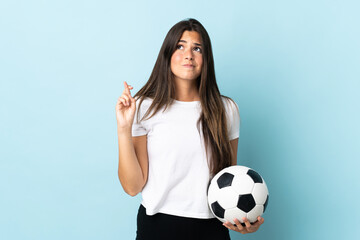 Young football player brazilian girl isolated on blue background with fingers crossing and wishing the best © luismolinero